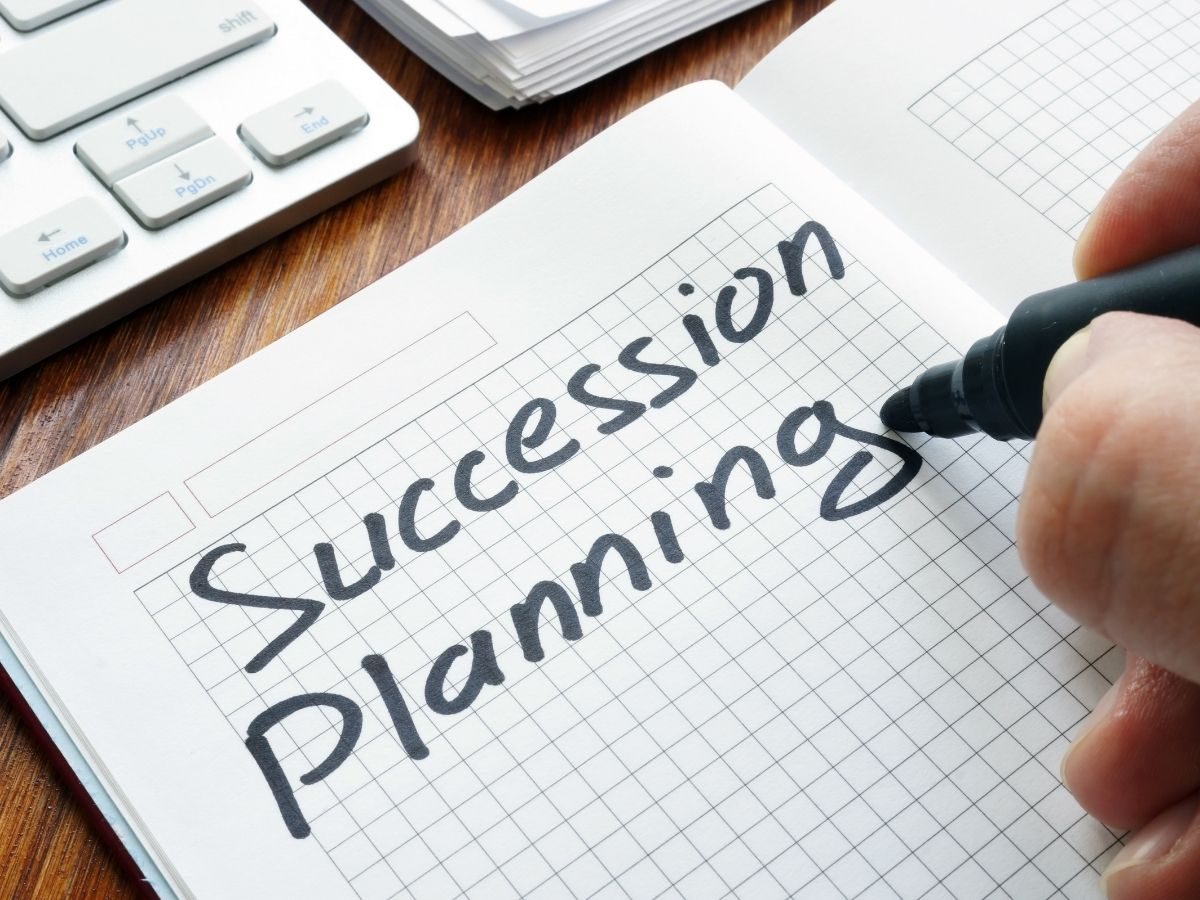 Mano escribiendo «Succession Planning» en un cuaderno
